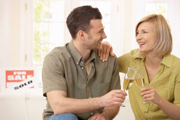 Two people drinking champaign with sold sign behind them