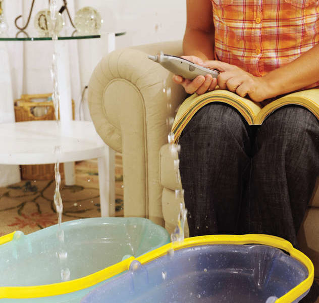 Person on phone with buckets of water filling up from water raining from ceiling